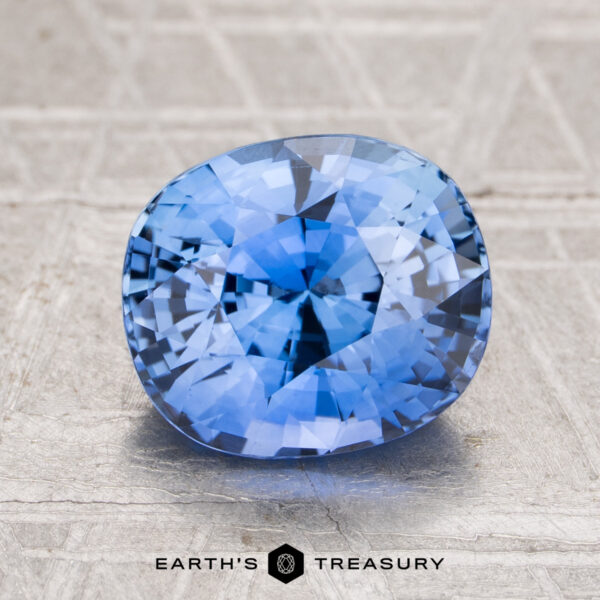 3.01-Carat Ceylon Sapphire (Heated) A 3.01-carat heated Ceylon sapphire with a cushion cut is displayed on a textured surface, with “Earth’s Treasury” shown below the gem.