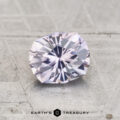A 1.04-carat Montana sapphire, faceted in an oval shape with light purple hues, displayed on a textured gray surface with "Earth's Treasury" below.