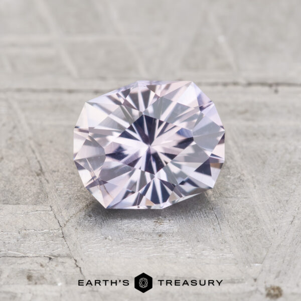 1.04-Carat Light Gray to Lilac Color-Change Montana Sapphire A 1.04-carat Montana sapphire, faceted in an oval shape with light purple hues, displayed on a textured gray surface with "Earth's Treasury" below.