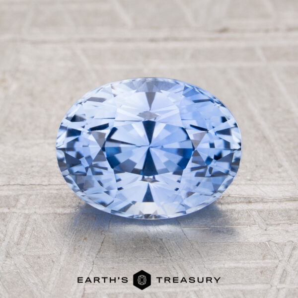 2.37-Carat Ceylon Sapphire (Heated) A 2.37-carat heated Ceylon sapphire, cut in a faceted oval, rests on a textured light surface with "EARTH'S TREASURY" displayed below.