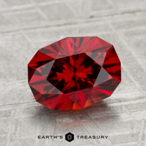 A 2.99-carat Spessartine Garnet with a brilliant cut is displayed on a textured, light gray surface. The Earth's Treasury logo appears at the bottom of the image.