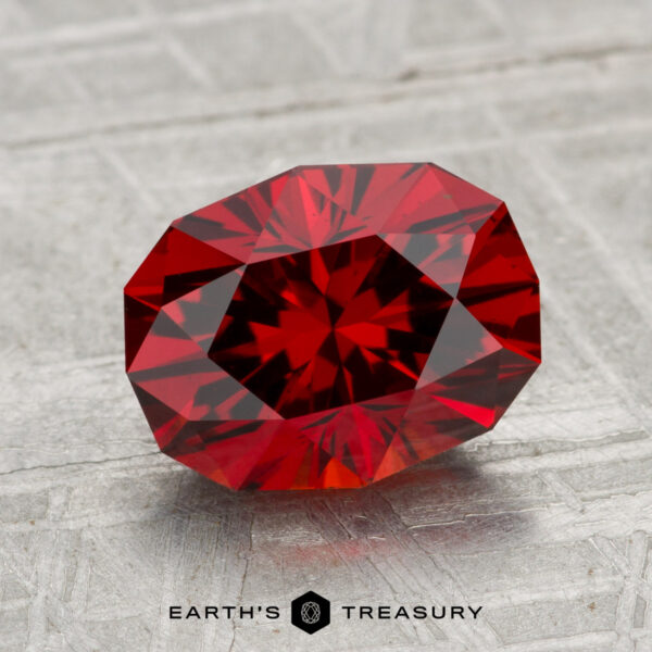 2.99-Carat Spessartine Garnet A 2.99-carat Spessartine Garnet with a brilliant cut is displayed on a textured, light gray surface. The Earth's Treasury logo appears at the bottom of the image.
