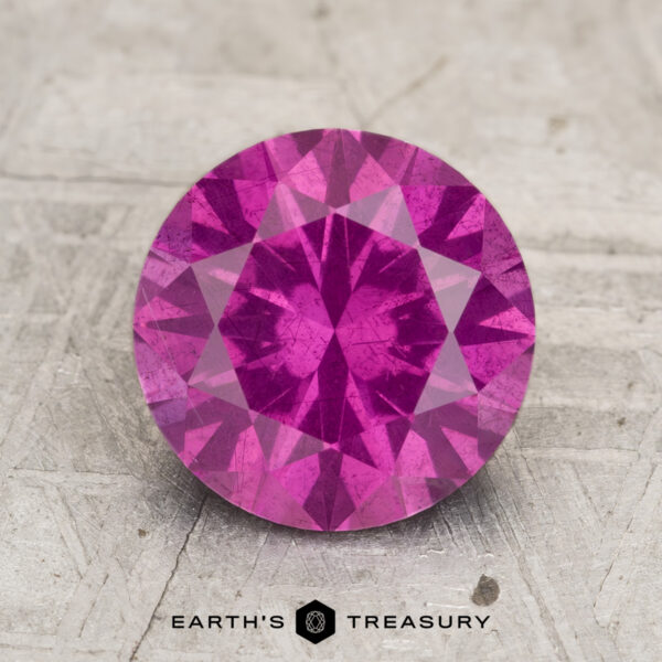 2.50-Carat Pastel Pyrope Garnet A 2.50-carat Pastel Pyrope Garnet, round and faceted, is displayed on a textured surface with the "EARTH'S TREASURY" logo underneath.