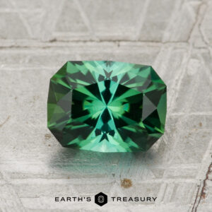 A 1.45-carat rectangular green tourmaline with intricate facets is shown on a textured background, with "EARTH'S TREASURY" written below.