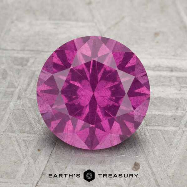 2.50-Carat Pastel Pyrope Garnet A round, faceted 2.50-carat pastel pyrope garnet is displayed on a textured surface with "EARTH'S TREASURY" written below.