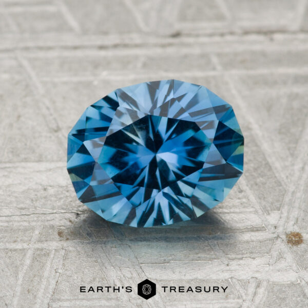 1.95-Carat Medium Blue Montana Sapphire A 1.95-carat Montana Sapphire, round brilliant-cut and blue, is displayed on a textured gray surface with "Earth's Treasury" below it.