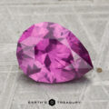 A 2.43-carat pastel pyrope garnet, cut in a faceted pear shape, rests on a textured grey surface with "EARTH'S TREASURY" displayed below.