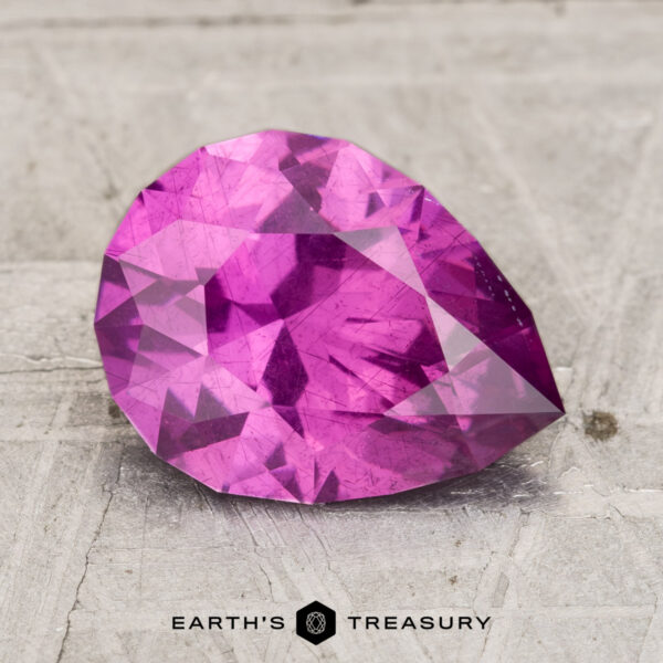 2.43-Carat Pastel Pyrope Garnet A 2.43-carat pastel pyrope garnet, faceted and vibrant pink, is displayed on a textured, light-colored surface with the text "Earth's Treasury" below.