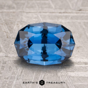A 2.63-carat heated sapphire is displayed on a textured light gray surface with the "Earth's Treasury" logo beneath it.