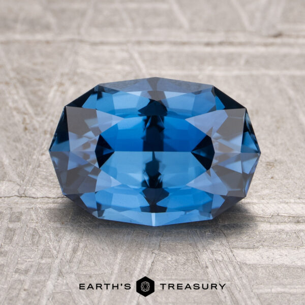 2.63-Carat Rich Blue Madagascar Sapphire (Heated) A 2.63-carat heated sapphire is displayed on a textured light gray surface with the "Earth's Treasury" logo beneath it.