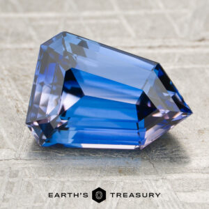 A 3.01-carat heated sapphire with angular facets rests on a textured surface, displayed above the Earth's Treasury logo and text.