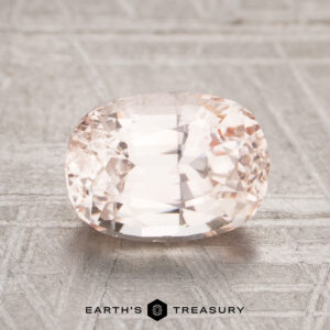 A 2.24-carat Ceylon sapphire, with a faceted light pink hue, rests on a textured metallic surface with "Earth's Treasury" displayed below.