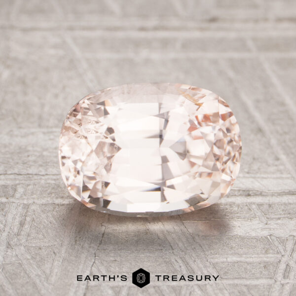 2.24-Carat Peach Unheated Ceylon Sapphire A 2.24-carat Ceylon sapphire, with a faceted light pink hue, rests on a textured metallic surface with "Earth's Treasury" displayed below.
