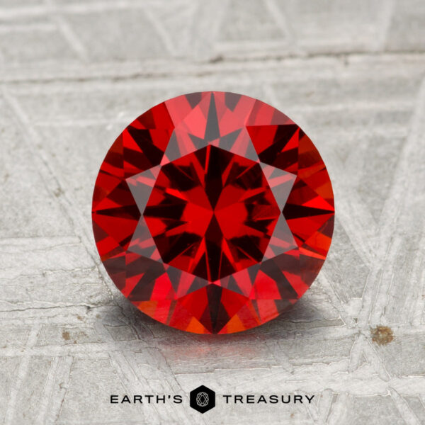 2.48-Carat Spessartine Garnet A 2.48-carat spessartine garnet, round brilliant-cut, displayed on a textured gray surface with "EARTH'S TREASURY" at the bottom.