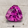 A vivid, triangular-cut 2.30-carat pastel pyrope garnet gemstone placed on a textured surface, with the text “Earth’s Treasury” at the bottom of the image.
