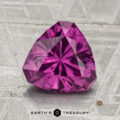 A 2.30-carat pastel pyrope garnet, trillion-cut and purplish-pink, rests on a textured gray surface with "Earth's Treasury" shown at the bottom.