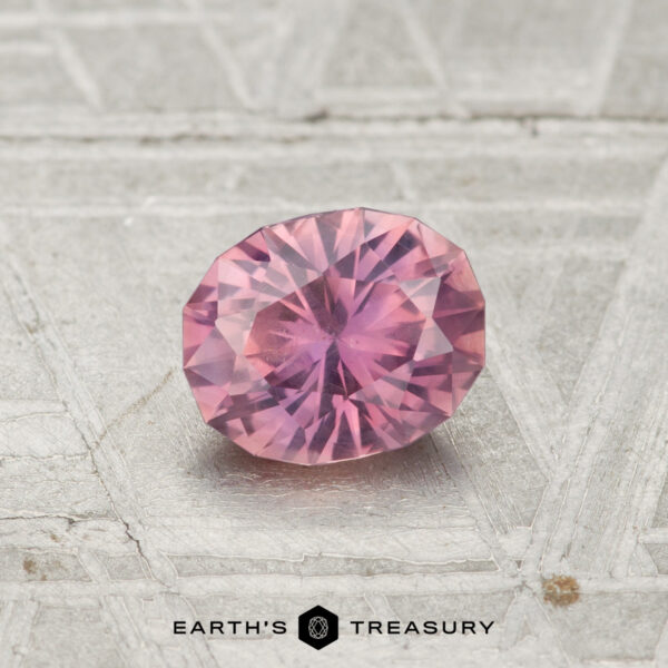 A 0.78-carat, faceted oval Montana sapphire is displayed on a textured metallic surface with the "Earth's Treasury" logo and text at the bottom.