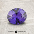A 1.46-carat unheated Ceylon sapphire with an oval cut is displayed on a textured gray surface, featuring the "Earth's Treasury" logo below.