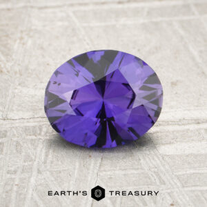 A 1.46-carat unheated Ceylon sapphire with an oval cut is displayed on a textured gray surface, featuring the "Earth's Treasury" logo below.