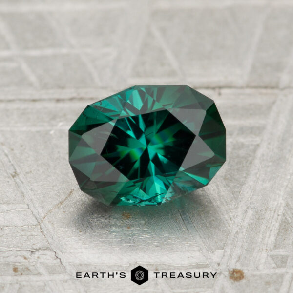 1.23-Carat Tourmaline A 1.23-carat faceted green tourmaline with a starburst pattern rests on a textured gray surface, with "Earth's Treasury" written below.
