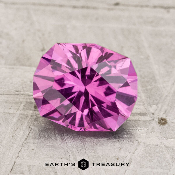 2.21-Carat Pastel Pyrope Garnet A faceted, round brilliant-cut 2.21-Carat Pastel Pyrope Garnet rests on a textured surface with the text "EARTH'S TREASURY" at the bottom.