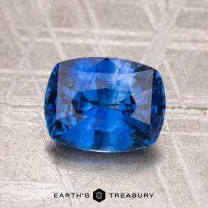 A 2.04-carat heated Ceylon sapphire rests on a textured metallic surface with the "Earth's Treasury" logo at the bottom.
