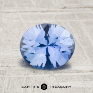 A 1.53-carat unheated Ceylon sapphire with an oval faceted cut is displayed on a light textured surface, with "Earth's Treasury" shown below.