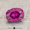 A 2.16-carat pastel Pyrope Garnet with an oval cut and multiple facets rests on a textured, light-colored surface above the "EARTH'S TREASURY" text.