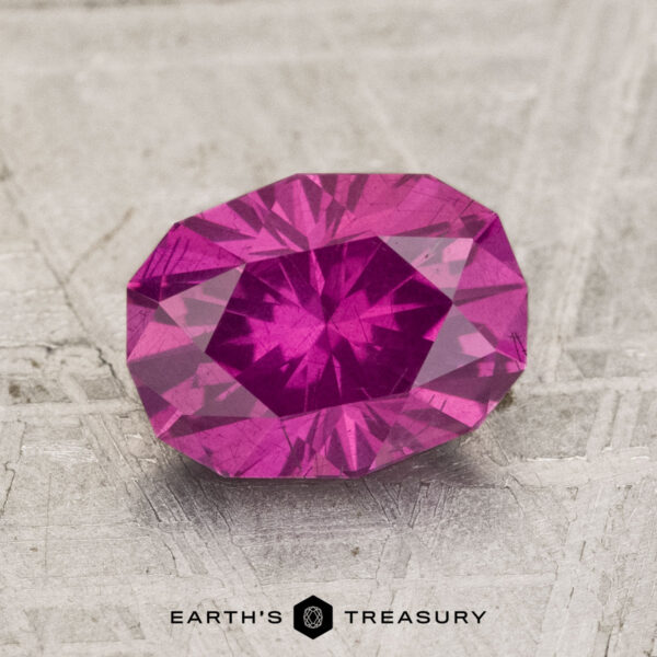 2.16-Carat Pastel Pyrope Garnet A 2.16-carat pastel Pyrope Garnet with an oval cut and multiple facets rests on a textured, light-colored surface above the "EARTH'S TREASURY" text.
