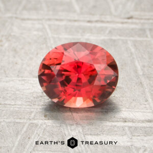 A 1.11-carat heated oval-cut sapphire with intricate facets rests on a textured gray surface, with "Earth's Treasury" displayed below.