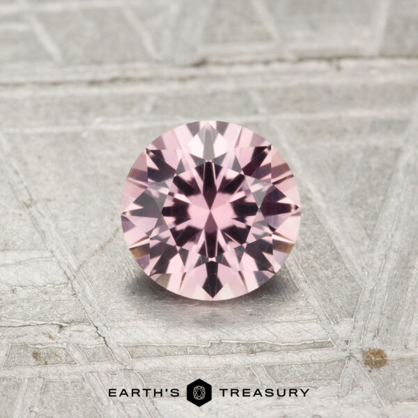 0.74-Carat Light Pink Montana Sapphire A 0.74-carat round-cut Montana sapphire shines on a textured gray surface with the "Earth's Treasury" logo at the bottom.