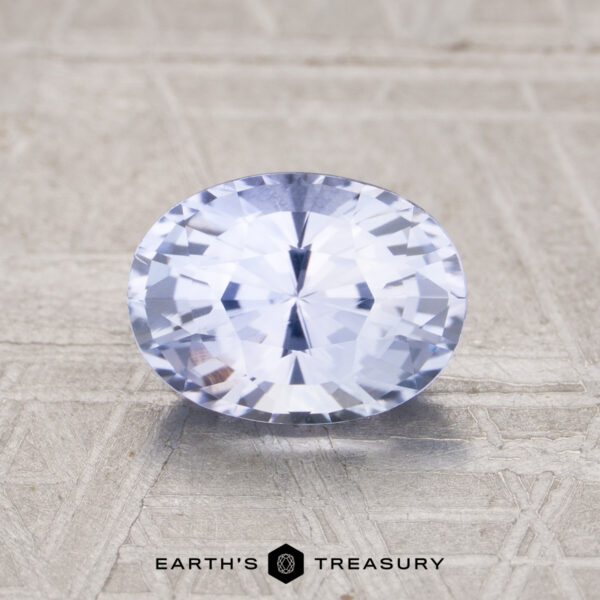 1.51-Carat Pale Violet-Blue Ceylon Sapphire A 1.51-carat Ceylon sapphire in an oval cut with a light lavender hue is shown on a textured surface, with the Earth's Treasury logo displayed below.