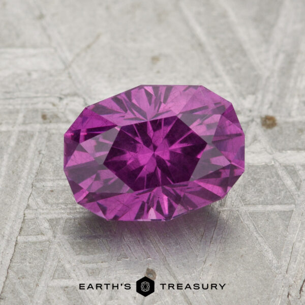 2.02-Carat Pastel Pyrope Garnet A faceted, oval-cut 2.02-carat pastel pyrope garnet rests on a textured metallic surface featuring the "Earth's Treasury" branding at the bottom.