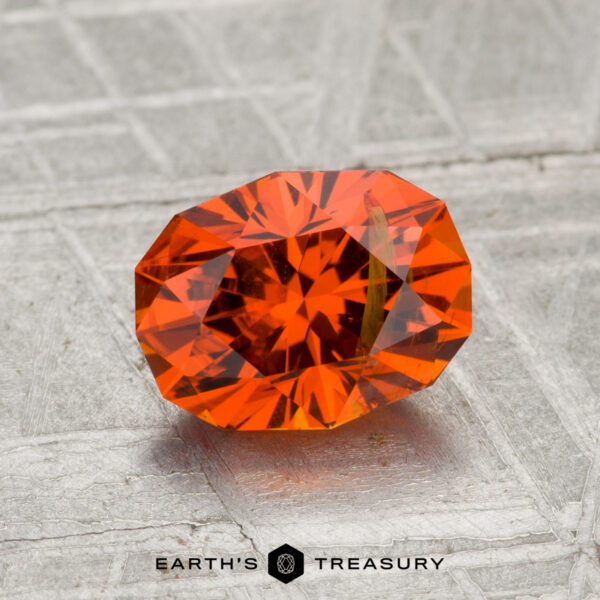 1.86-Carat Spessartine Garnet A 1.86-carat faceted spessartine garnet with a brilliant cut is displayed on a textured gray surface, with the "Earth's Treasury" logo at the bottom.
