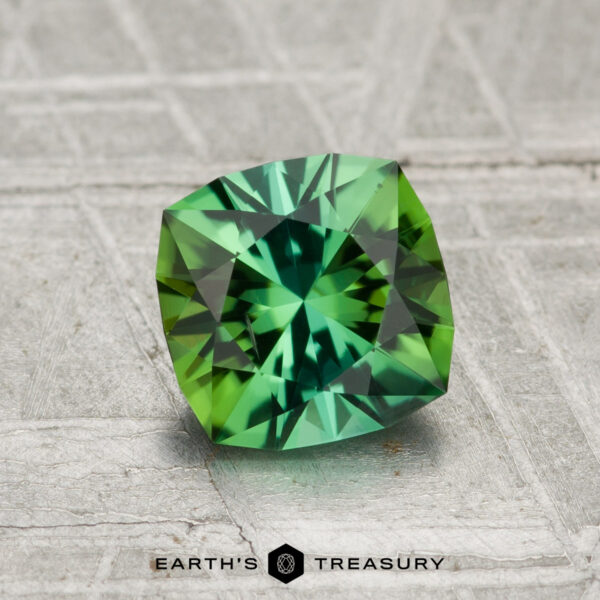 1.09-Carat Tourmaline A faceted green 1.09-carat tourmaline with a square cushion cut rests on a textured gray surface; "Earth's Treasury" is printed at the bottom.