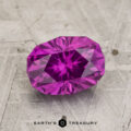 A 2.02-carat Pastel Pyrope Garnet with an oval faceted cut rests on a textured gray surface, featuring "EARTH'S TREASURY" at the bottom.