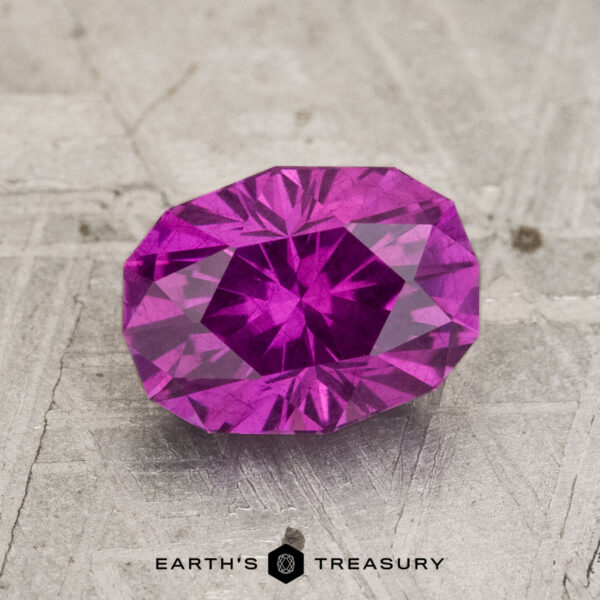 2.02-Carat Pastel Pyrope Garnet A 2.02-carat Pastel Pyrope Garnet with an oval faceted cut rests on a textured gray surface, featuring "EARTH'S TREASURY" at the bottom.