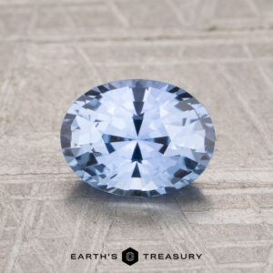 1.48-Carat Ceylon Sapphire, oval-cut blue gemstone, showcased on a textured beige surface with the "Earth's Treasury" logo at the bottom.