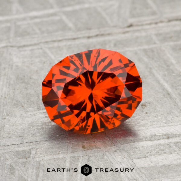 1.83-Carat Spessartine Garnet A 1.83-carat faceted, oval-cut Spessartine garnet with a vivid orange hue displayed on a textured gray surface, featuring the "Earth's Treasury" text at the bottom.