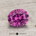 A 2.01-carat pastel pyrope garnet gemstone sits on a textured, light gray surface with "EARTH'S TREASURY" displayed at the bottom.
