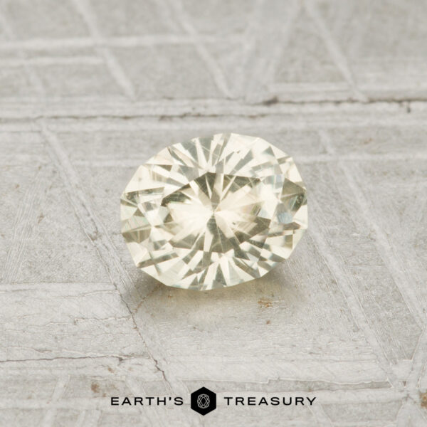 0.74-Carat Pale Yellow Montana Sapphire A 0.74-carat Montana sapphire with an oval cut and yellow hue is displayed on a textured gray surface, featuring the text "EARTH'S TREASURY" at the bottom.