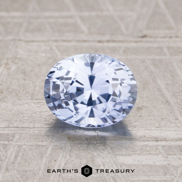 1.34-Carat Pale Violet-Blue Ceylon Sapphire A 1.34-carat Ceylon sapphire, oval-cut and pale blue, rests on a textured surface with "EARTH'S TREASURY" below it.