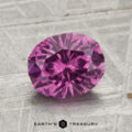 A 2.01-carat pastel pyrope garnet, faceted in an oval cut, is displayed on a textured gray surface with the words "EARTH'S TREASURY" at the bottom.