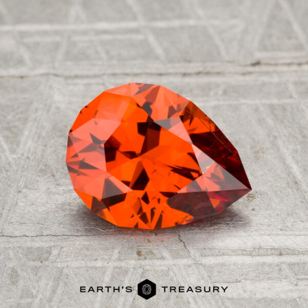 1.73-Carat Spessartine Garnet A 1.73-carat Spessartine Garnet, pear-shaped and faceted in orange, rests on a textured gray surface with "EARTH'S TREASURY" displayed below.