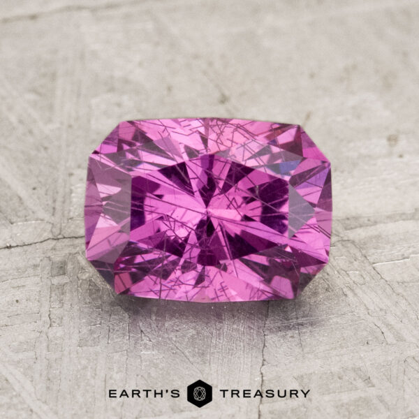 2.01-Carat Pastel Pyrope Garnet A 2.01-carat Pastel Pyrope Garnet with a rectangular radiant cut and visible internal inclusions, shown on a textured gray surface with "EARTH'S TREASURY" beneath it.