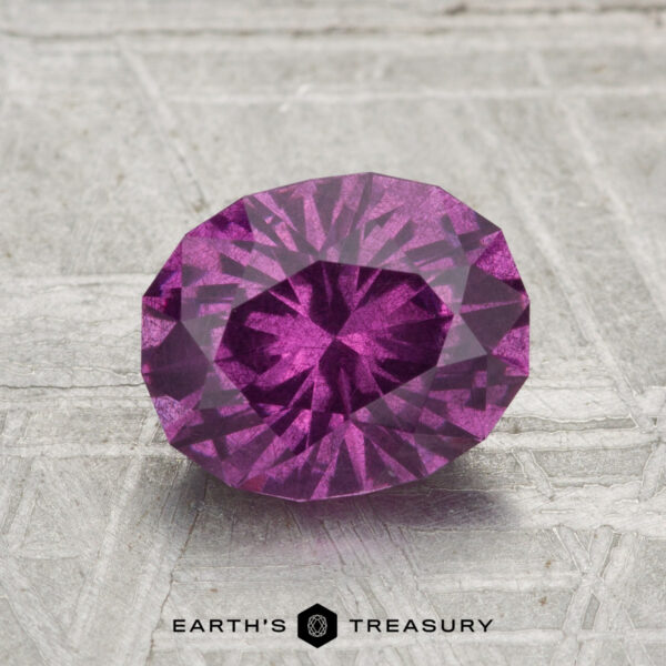 1.92-Carat Pastel Pyrope Garnet A 1.92-carat pastel pyrope garnet with an oval cut is displayed on a gray textured surface, featuring the "EARTH'S TREASURY" text at the bottom.