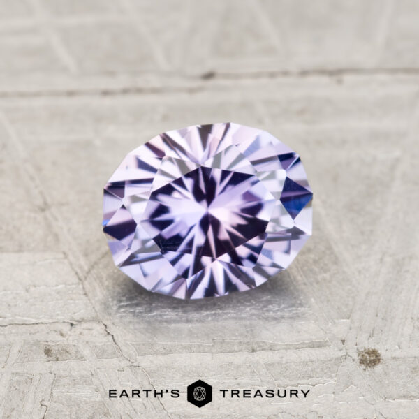 1.21-Carat Light Violet to Purple Color-Change Montana Sapphire A 1.21-carat Montana sapphire, faceted in an oval cut with pale purple and blue hues, rests on a textured light gray surface with "EARTH'S TREASURY" displayed below.