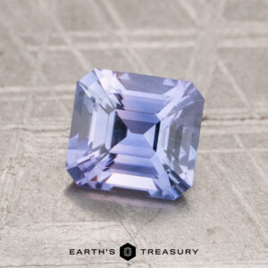 A square-cut, faceted 1.66-carat Ceylon Sapphire with a light purple hue is displayed on a textured, light-colored surface featuring the "EARTH'S TREASURY" logo and text below it.
