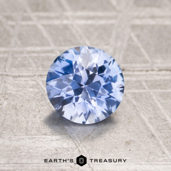 1.09-Carat Ceylon Sapphire A 1.09-carat Ceylon sapphire, round brilliant-cut and blue, is displayed on a textured, light-colored surface with “EARTH’S TREASURY” at the bottom.