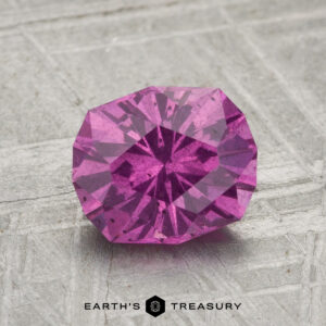 A 1.91-carat pastel pyrope garnet, round-cut and faceted, is shown on a textured gray background with "EARTH'S TREASURY" displayed at the bottom.